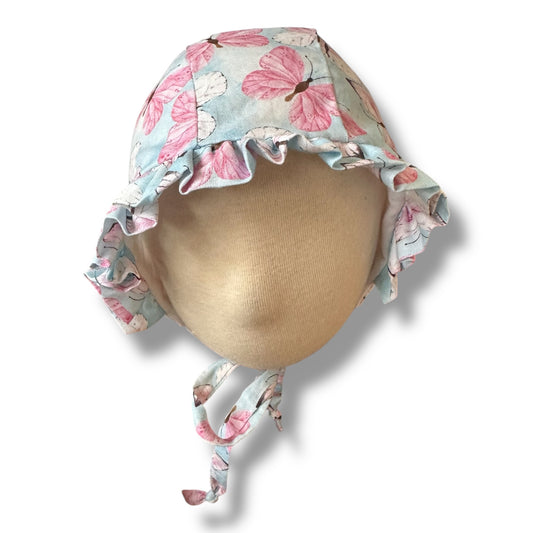 A handmade baby ruffle bonnet in baby blue with pink and white butterfly print, on a mannequin head against a white background