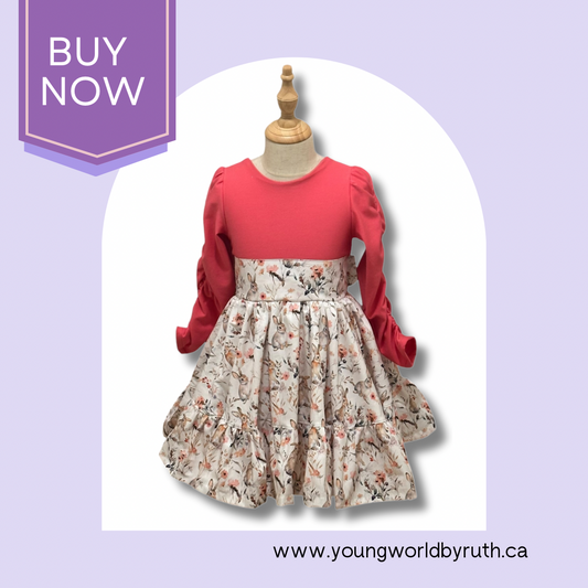 A girl's dress with a coral colored bodice and a bunny-print skirt, featuring long sleeves and a bow at the back, displayed on a mannequin.