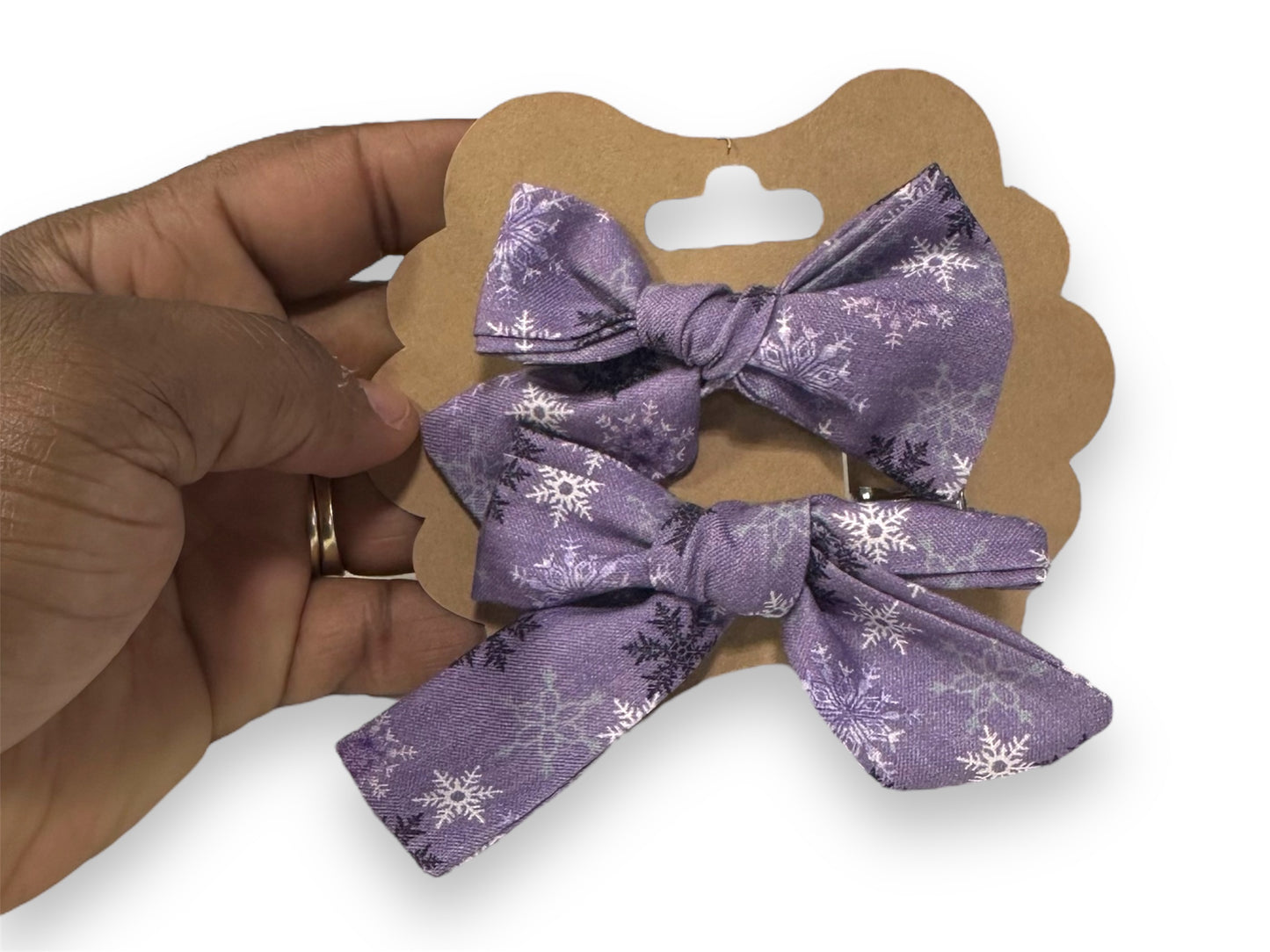 A mini hair bow set with a purple bow featuring white snowflake patterns, held in a person's hand.