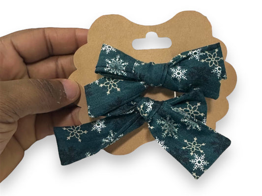 A mini hair bow set with a green bow featuring white snowflake patterns, held in a person's hand.