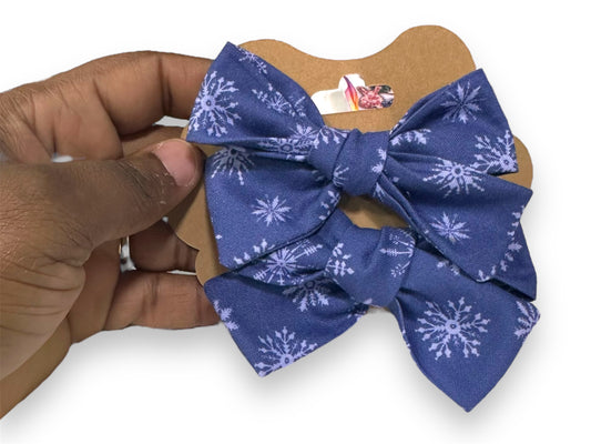A mini hair bow set with a blue bow featuring white snowflake patterns, held in a person's hand.