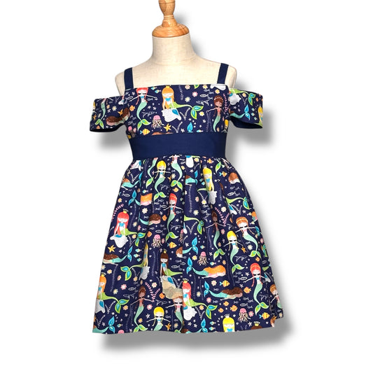 A handmade navy dress with a colorful mermaid print, featuring off-the-shoulder sleeves and a navy waistband on a mannequin.
