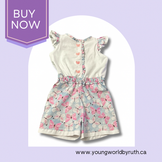A Handmade romper with a whimsical butterfly pattern, featuring flutter sleeves, a ruche waistband, and front button closure on a light purple background with a BUY NOW sign at the top left corner.