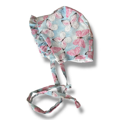 A Handmade baby bonnet  in baby blue with pink butterfly pattern on a white background