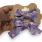 A mini hair bow set with a purple bow featuring white snowflake patterns, held in a person's hand.