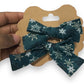A mini hair bow set with a green bow featuring white snowflake patterns, held in a person's hand.