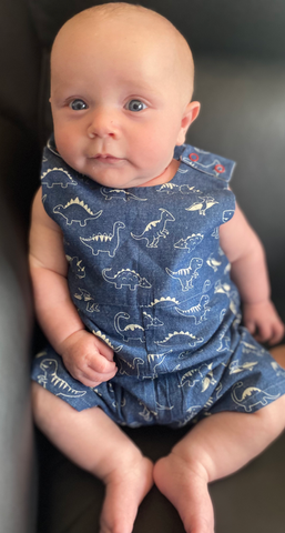 Baby wearing a blue romper with dinosaur patterns on a dark background